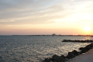 Sahilde romantik bir gün batımı. Deniz limanı arka planında derin mavi bir su.