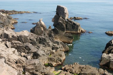 sunny lonely beach with deep blooming water and boulders and rocks 