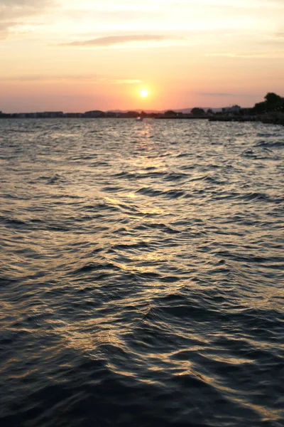 海港を背景に深い青の海が広がる海岸沿いの美しい夕日 — ストック写真