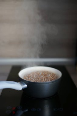 boiling buckwheat in saucepan on electric black stove with glossy surface