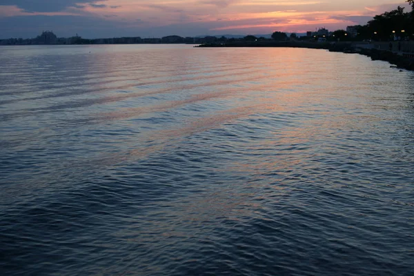 海港を背景に深い青の海が広がる海岸の素晴らしい夕日 — ストック写真