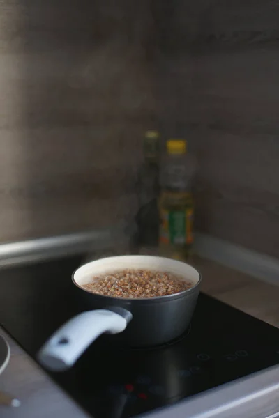 boiling buckwheat in saucepan on electric black stove with glossy surface