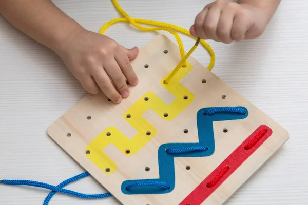 Çocuk ahşap renkli tahta ve bağcıklarla eğitici oyunlar oynuyor. Geliştirme, eğitim.