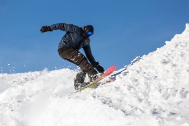 Snowboardcu dağlardaki karlı bir pistte atlayış yapıyor. Kış sporları.