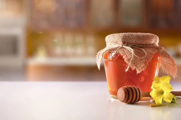 Glasgefäß mit Honig und Löffel auf weißem Küchentisch — Stockfoto
