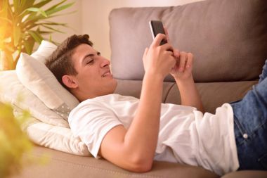 Yüz bir smartphone kullanarak kanepeye gülümseyen genç
