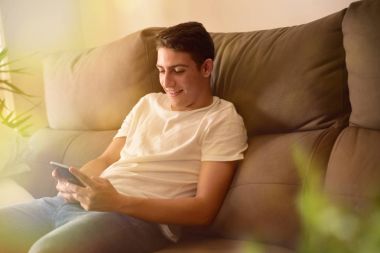 Bir smartphone kullanarak kanepede oturan gülümseyen genç