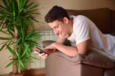 Genç çocuk gülümseyen yüzü aşağı bir smartphone danışmanlık kanepede