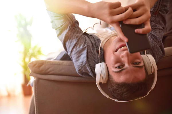 Έφηβος/η που βρίσκεται μπρούμυτα στον καναπέ ακούγοντας μουσική με οπίσθιο φωτισμό — Φωτογραφία Αρχείου