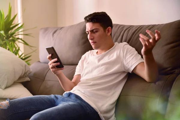 Teenager i uenighed med nyheder på smartphone på sofaen - Stock-foto