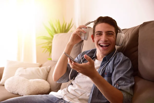 Tinédzser nevetve a fejhallgató ül a kanapén látszó egyenes — Stock Fotó