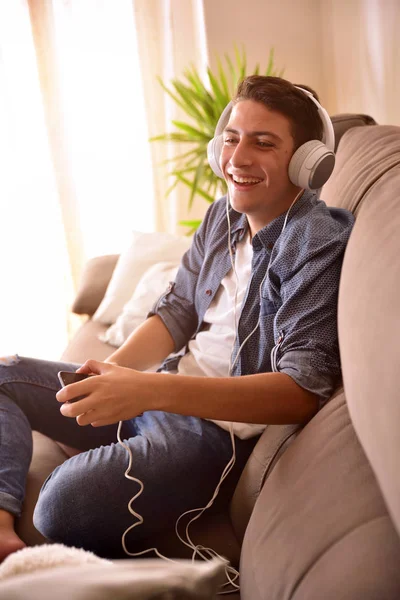 Tinédzser nevetve-a smartphone és a fejhallgatót a fotelben függ — Stock Fotó