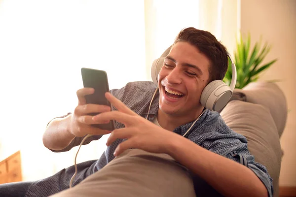 Teenager griner med smartphone lænet på bagsiden af sofaen - Stock-foto