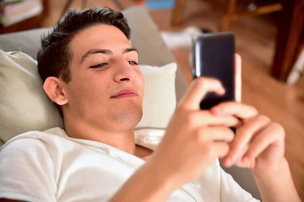 Fiatal fiú felfelé a kanapén játszik egy smartphone — Stock Fotó