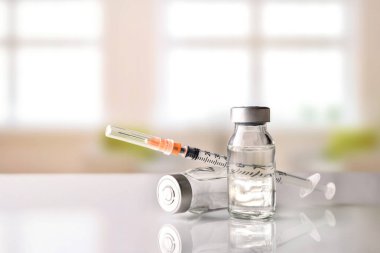 Vials and syringe on white table with background windows clipart