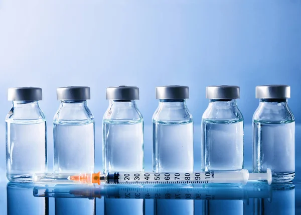 Row of vials and syringe on blue table front view — Stock Photo, Image