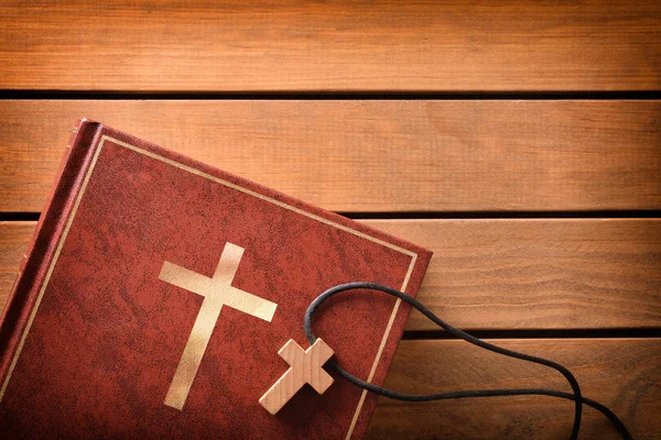 Библия с крестообразным кулоном на деревянном столе — стоковое фото