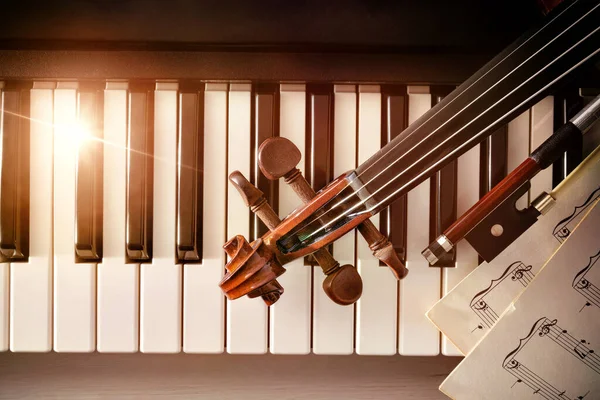 Violin pegbox bow and sheet music on piano keys top — Stock Photo, Image