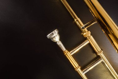 Ağızlığın ve trombon tellerinin ayrıntıları siyah ahşap masada. Üst Manzara. Yatay bileşim.
