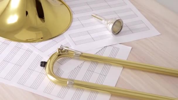 Trombone dorato smontato e partiture su tavola in legno vista rotante — Video Stock
