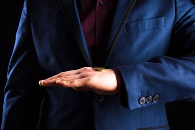 Mor takım elbiseli bir işadamı avucunda sarı bir para tutar.