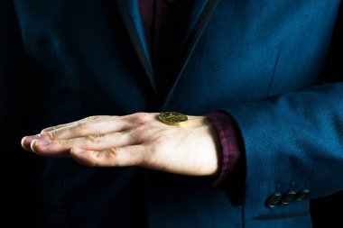 Mor takım elbiseli bir işadamı avucunda sarı bir para tutar.