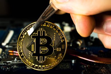 Bilgisayar panosundaki Bitcoin. Bir adam bitcoin 'i cımbızla tutar.