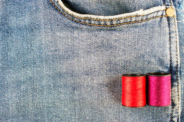 Threads on the background of jeans. Blue and red thread on the background of blue jeans.