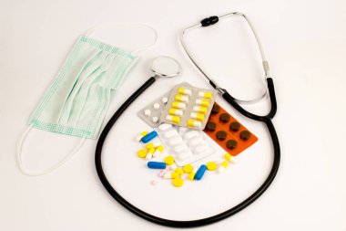 Beyaz arka planda anti virüs maskesi ve steteskop. Haplar beyaz masaya saçılmış.. 