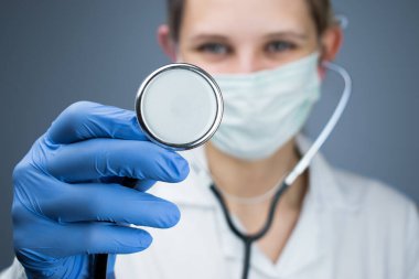 Sabahlık giymiş bir doktor steteskop gösteriyor..