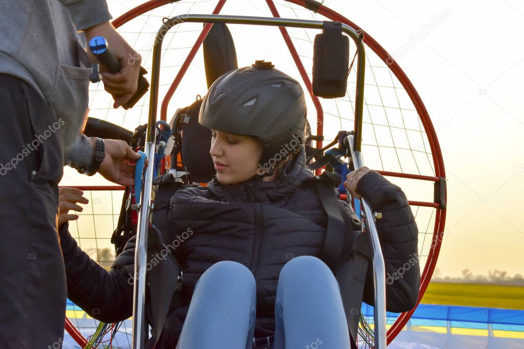 The girl is preparing to fly on a hang glider. The girl is sitting in the passenger seat of a motor hang glider.