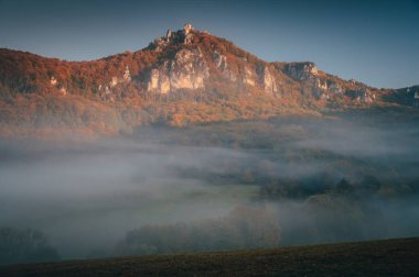 Sıra dışı sihirli sonbahar manzarası. Çayırlarda sis ve arka planda kayalık tepeler