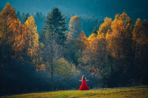 Γυναίκα με κόκκινο φόρεμα στέκεται στην όμορφη φύση του φθινοπώρου — Φωτογραφία Αρχείου
