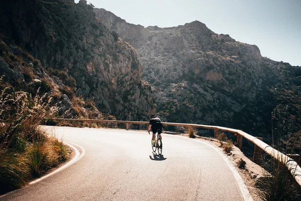 Solo uomo su strada giro in bicicletta in salita in grandi montagne. Luce arancio tramonto sullo sfondo — Foto Stock