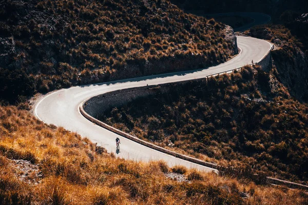 Road biker silhouette on the road in mountains. Sport cycling photo. — ストック写真