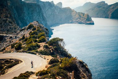 Yalnız bisikletçi silueti deniz kenarındaki yolda. Arka planda güzel doğa.