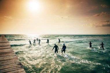 Triatlonun başında dalgıç kıyafetli yarışmacılar suya koşuyor. Mallorca 'da deniz, arka planda gün batımı ışığı