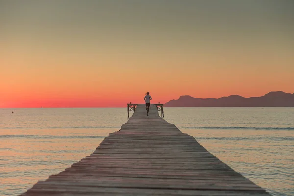 Frau läuft auf Holzsteg. Sonnenaufgang Meereslandschaft im Hintergrund — Stockfoto