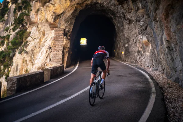 山の中で道路上の自転車に乗るの男。道路上の暗い岩のトンネル。Sa Calobra,マヨルカ島,スペイン — ストック写真