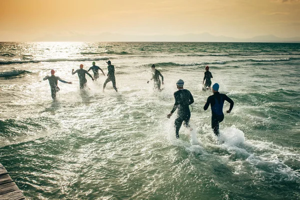 Begynnelsen på en triatlon. Silhouette av konkurrenter i våtdrakter, som løper ut i vannet – stockfoto