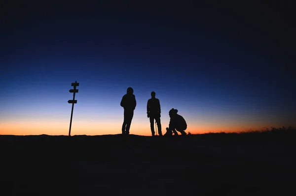 Drei Touristen, die auf dem Kamm der Morgenberge stehen. Sonnenaufgangsfarben im Hintergrund — Stockfoto