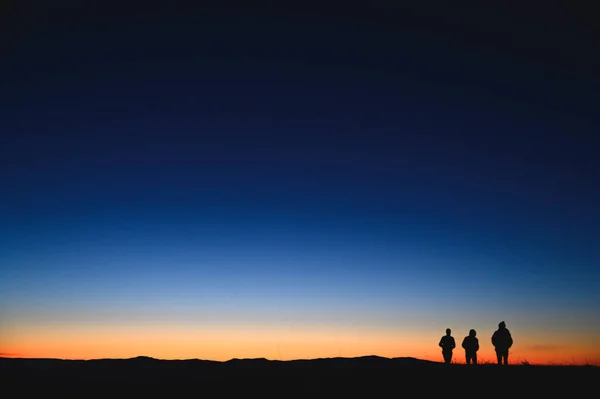 Tres turistas caminando por las montañas de la mañana. Colores del amanecer en fondo — Foto de Stock