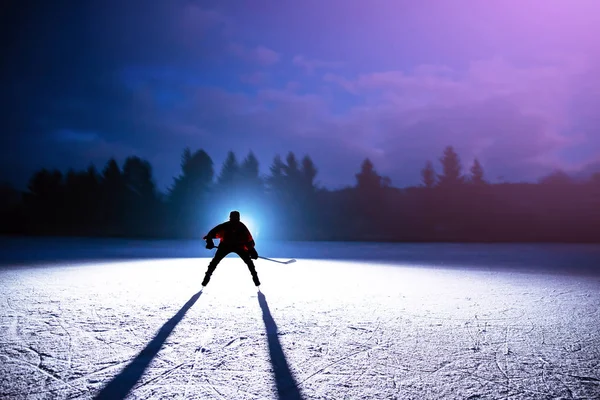Jovem jogador de hóquei silhueta no gelo da noite — Fotografia de Stock