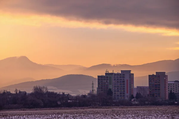 City in the cold winter morning, block of flats and orange sunrise light, hills and clouds in background — Stock Photo, Image