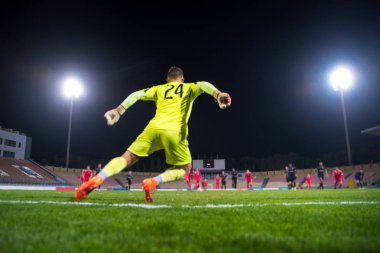 Topu yakalayan kaleci, gece futbol maçı, stadyum, spot ışıkları.