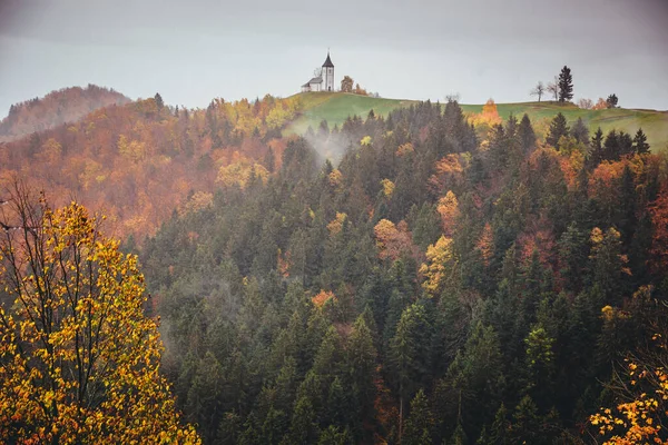 Mały romantyczny kościół na szczycie wzgórza w deszczowe kolorowe jesiennej przyrody. Jamnik, Słowenia, Europa — Zdjęcie stockowe