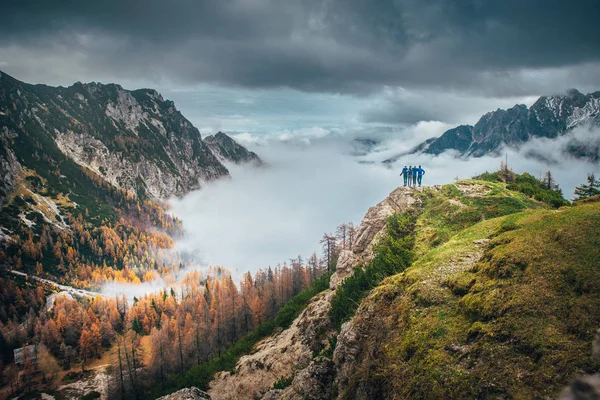 Grupp om fyra pojkar tillsammans i bergen. Vänner står tillsammans på toppen av den gröna kullen och tittar på magiska höstlandskap, dimma och stora berg. Vänskap, vandring inspirerande foto. — Stockfoto