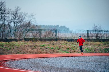 Tıbbi maske takan bir kaçakçı, Avrupa 'da Coronavirus salgını Covid-19. Spor, karantinada aktif yaşam yüz maskesi korumalı cerrahi sterilizasyon. Corona Salgını 'nda atletizm pistinde açık hava koşusu