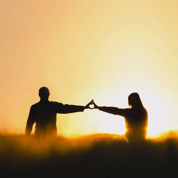 Silhouette of couple in love in beautiful morning wheat field, shape of heart from hands. Valentine photo full of love
