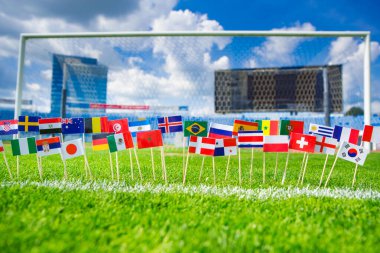 Tüm uluslar yeşil futbol çimlerinin üzerinde bayrak sallıyor. Arka planda futbol ağı ve mavi gökyüzü